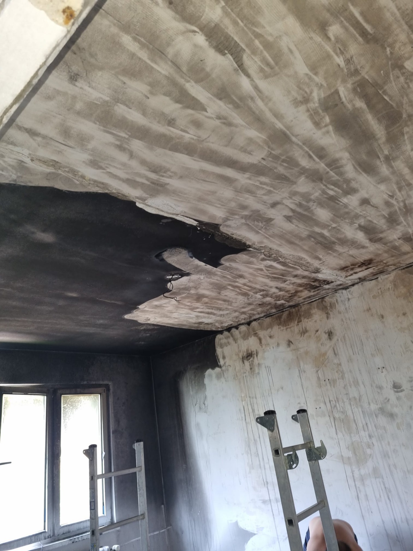 Pracovník při sanaci očouzeného interiéru s poškozeným stropem a stěnami